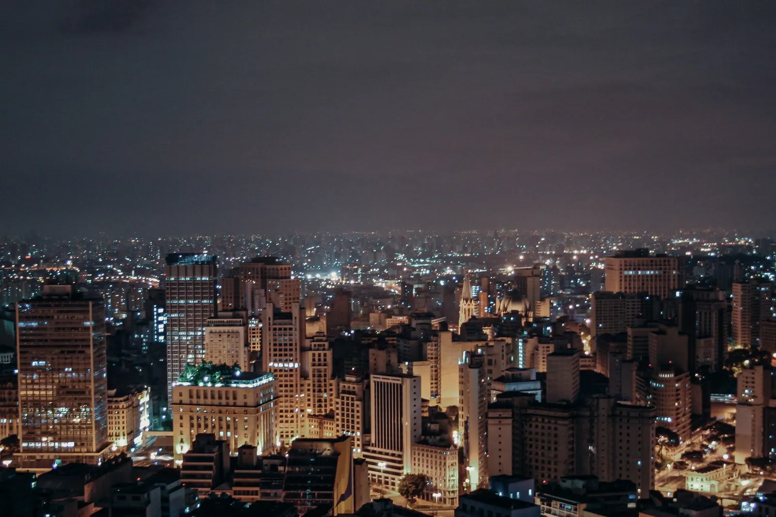 Vista aérea de uma cidade iluminada à noite. Imagem ilustrativa.